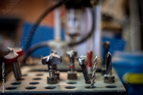 Selective blur on several drills used for woodworking in a carpenter workshop, in the middle of other components and parts used for drilling at a professional level.