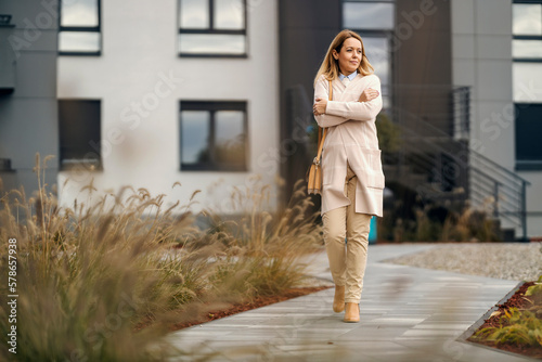 A woman in smart causal is walking on chilly weather on a street downtown.