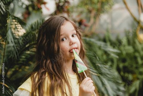 Cute little girl eating a watermelon shaped lollipop Child with lollipops in the botanical garden.