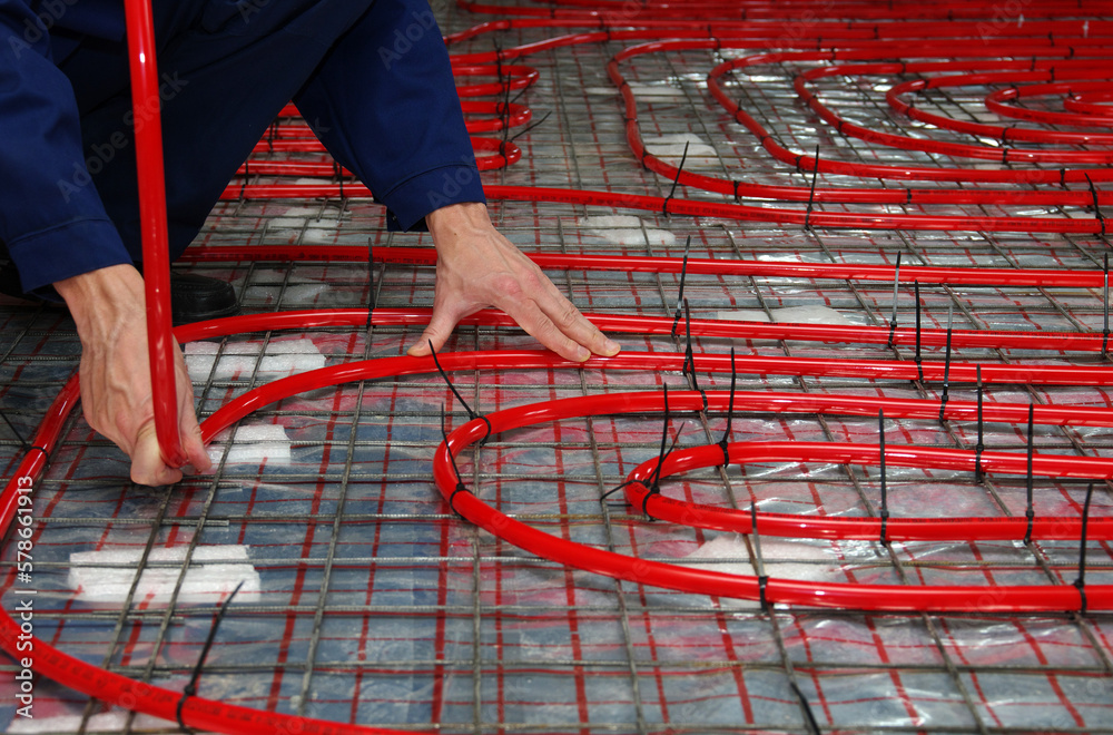 Naklejka premium Worker is installing a red pipe for underfloor heating