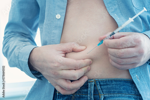 Diabetes patient insulin shot by syringe with dose of lantus, subcutaneous abdomen vaccination on blue background photo