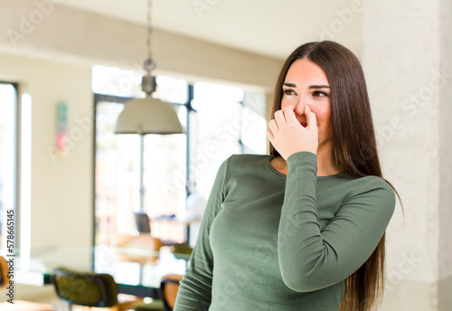 young adult pretty woman feeling disgusted, holding nose to avoid smelling a foul and unpleasant stench photo