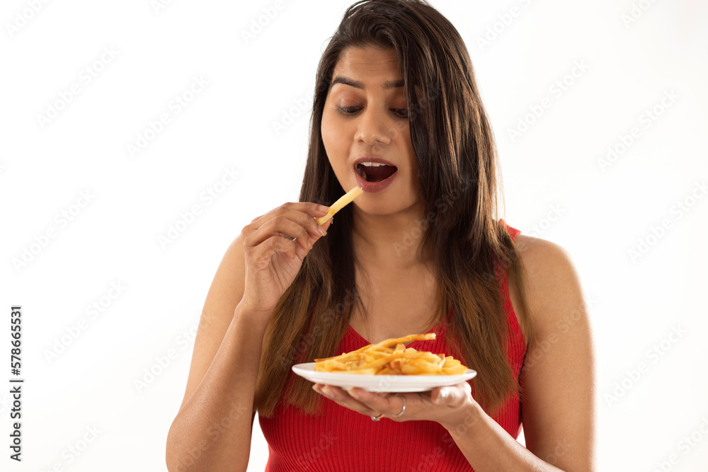 Close-up portrait of woman eating french fries against white background Close-up portrait of woman eating french fries against white background