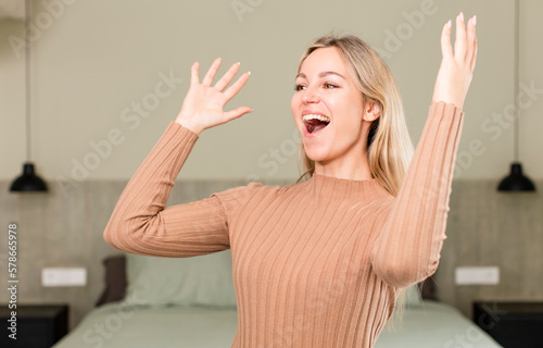 young pretty woman feeling happy, amazed, lucky and surprised, celebrating victory with both hands up in the air. bed concept