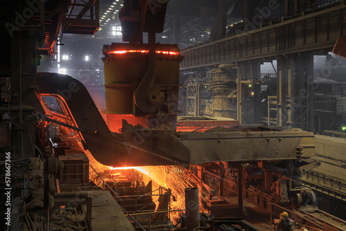 Hot steel pouring from big casting ladle into a mold in an iron foundry.
