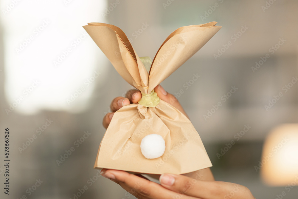 Obraz premium Easter Gifts Ideas. Female Hands Holding Bunny Shaped Craft Paper Bag