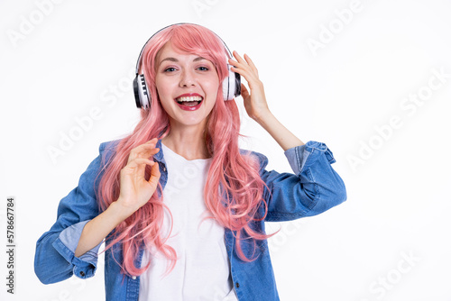Portrait of delighted woman in pink wig wearing headphones looking at camera posing in denim clothes and white t-shirt cheerful young girl having fun while shooting process.