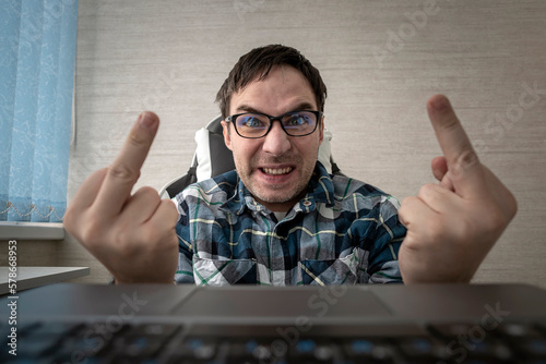man writes comments while sitting at a laptop and shows his middle finger at a computer screen monitor. insulting and bullying in comments and chats on the Internet. Fuck you sign. photo