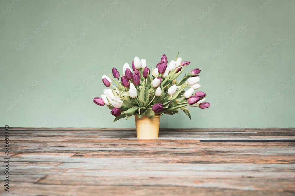 Bouquet of tulips in a yellow bucket in front of a green wall on wooden floor