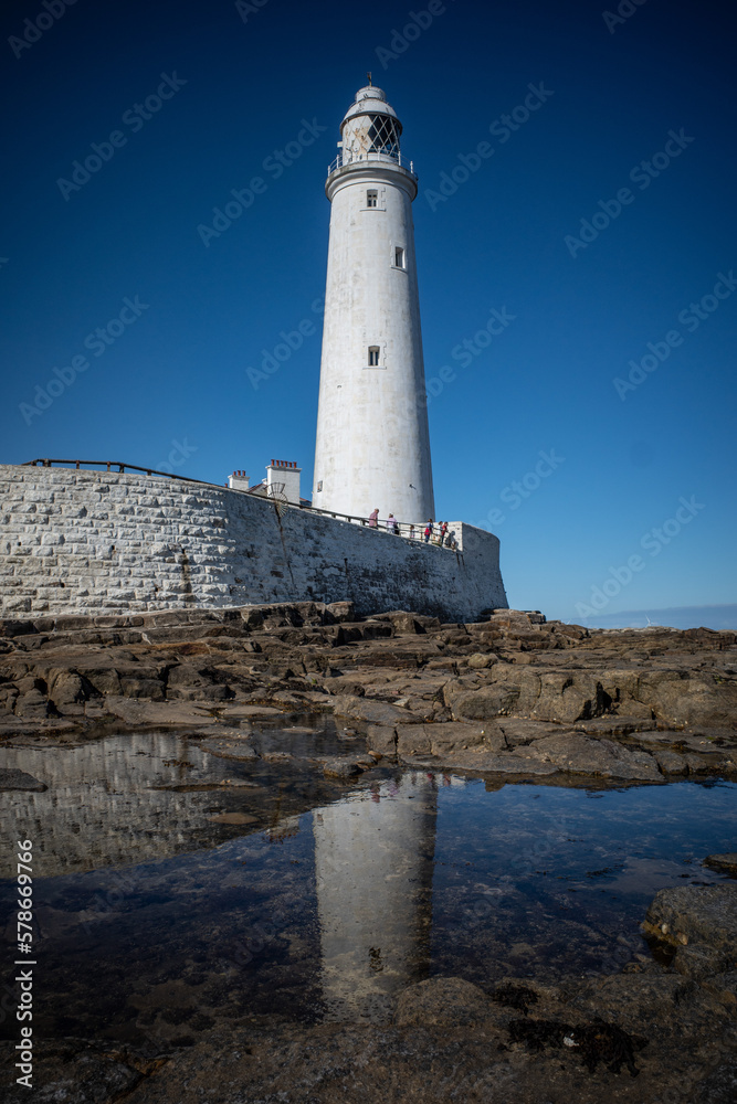 St Mary's Lighthouse on the coast under the blue sky and its reflection on the surface of water