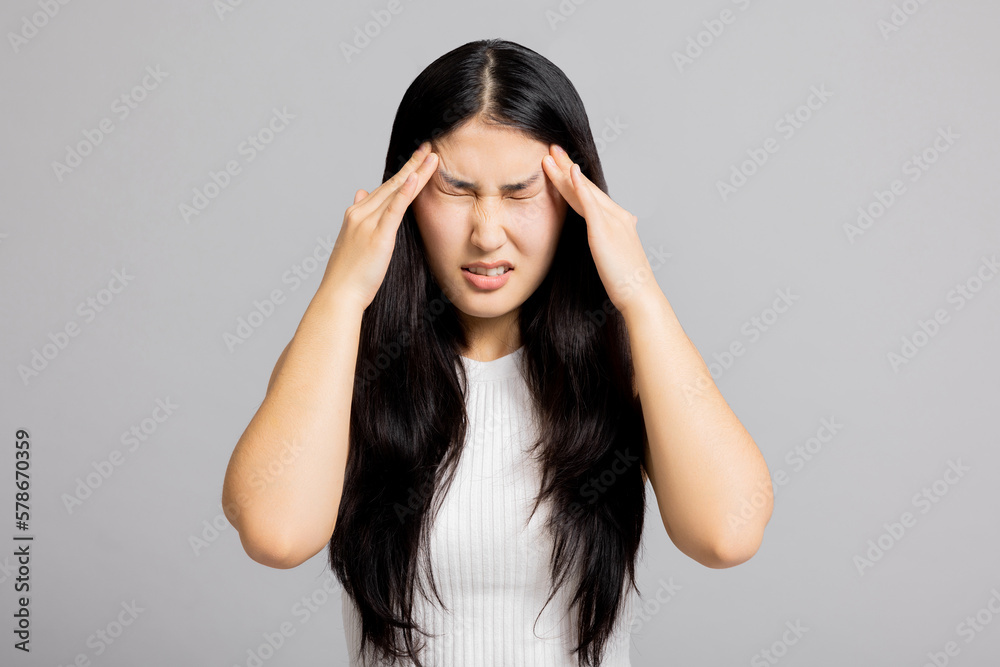 Sad exhausted young asian girl woman with headache suffering from migraine standing on grey background in studio isolated closing eyes holding arm near head. Sad exhausted young asian girl woman with headache suffering from migraine standing on grey background in studio isolated closing eyes holding arm near head.