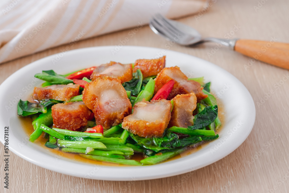 Stir fried kale with crispy pork in oyster sauce on white plate