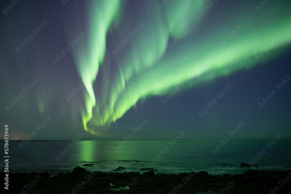 Aurora borealis branching out, reflecting over ocean beach Iceland