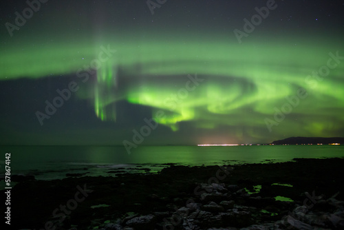 Aurora borealis reflecting over ocean and city Reykjavik Iceland