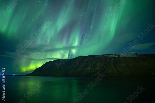 Bright full sky aurora borealis reflecting in ocean fjord Iceland