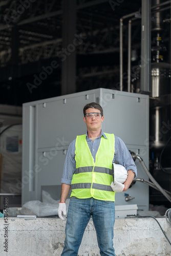 Portrait of a Professional American Heavy Industry Engineer Wearing Safety Uniform, Glasses, Hard Hat, Looking into the Camera. Confident American Industrial Specialist Standing in a Factory Facility