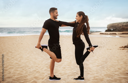 Couple in black sportswear training by seaside, doing stretching exercises for legs, standing in front of each other