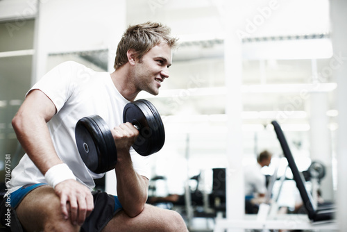 My biceps better bulge when Im done. a handsome young man working out with a dumbbell in the gym.