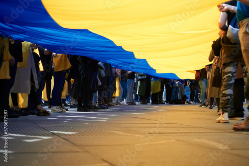 A crowd of people holding a large national Ukrainian flag at a peaceful demonstration in support of Ukraine against Russia's military aggression