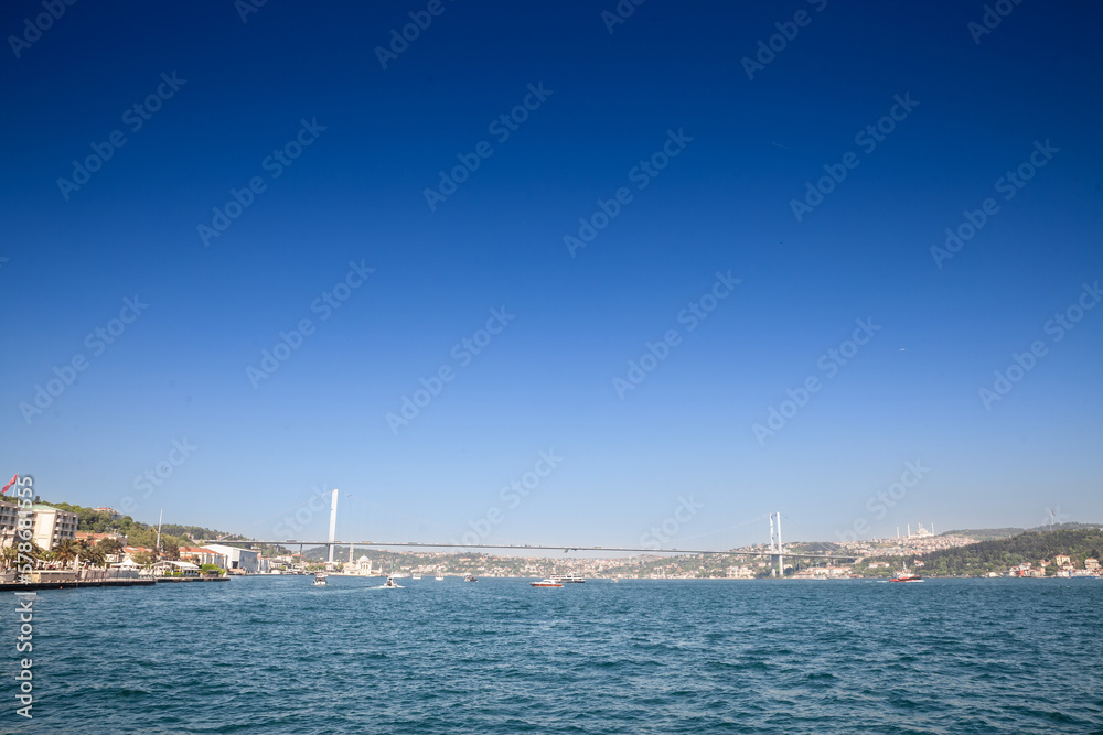 Bosphorus Bridge; also called 15 july martyrs bridge or 15 temmuz sehitler koprusu, seen from afar with boats passing on posporus strait. it's a bridge in Istanbul connecting Asian and European side.