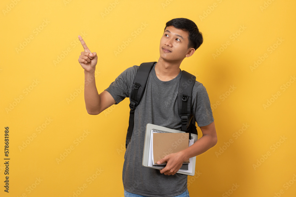 Smiling young college student with books and backpack isolated on yellow background pointing with fingers to the side present a product