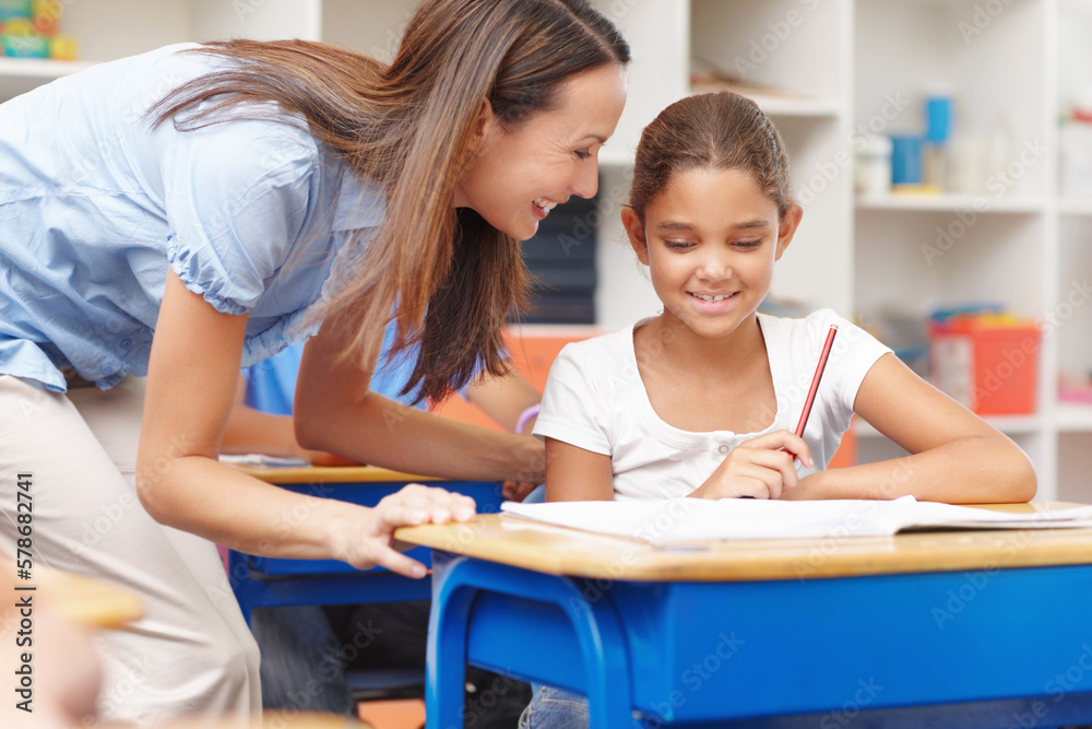 Proud of her star pupil. A pretty young teacher helping out a student with her work. Proud of her star pupil. A pretty young teacher helping out a student with her work.
