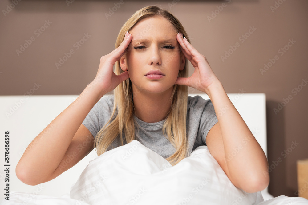 Pretty young blond woman lady in bedroom sitting on bed leaning on hand suffering from migraine pain having headache illness. Stressgul girl after hard day. Pretty young blond woman lady in bedroom sitting on bed leaning on hand suffering from migraine pain having headache illness. Stressgul girl after hard day.
