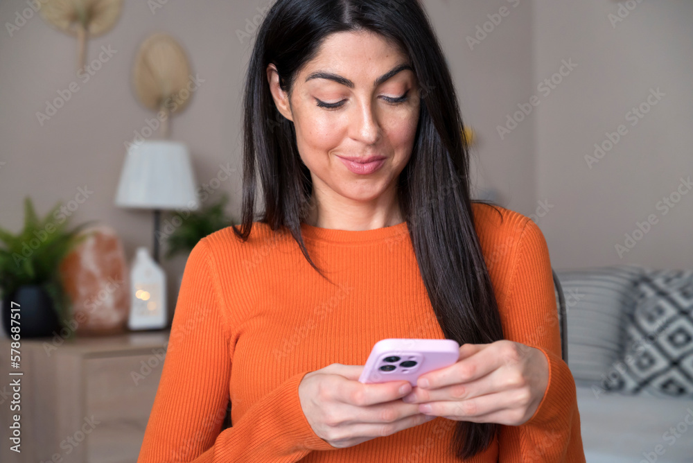 Beautiful young smiling woman sitting at home and using mobile phone Beautiful young smiling woman sitting at home and using mobile phone