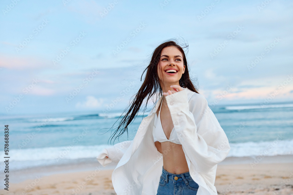 Brunette woman with long hair in a white shirt and jean shorts tan and  happy running