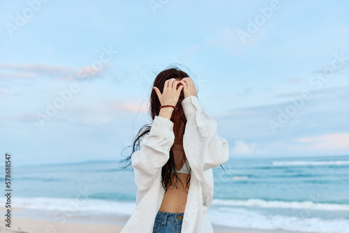 Brunette woman with long hair in a white shirt and shorts smile and happiness walking on the beach and having fun smile with teeth pulling hands into the camera selfies ocean, vacation summer travel