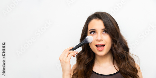 Portrait of a surprised woman applying face powder on the banner with copy space. 