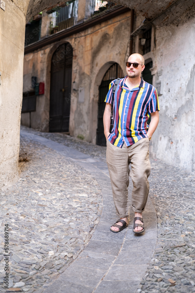 A man in a colorful shirt and loose pants enjoys his vacation in the south of Italy. He strolls through the streets and has an old black camera with him. He looks relaxed and in a good mood. A man in a colorful shirt and loose pants enjoys his vacation in the south of Italy. He strolls through the streets and has an old black camera with him. He looks relaxed and in a good mood.
