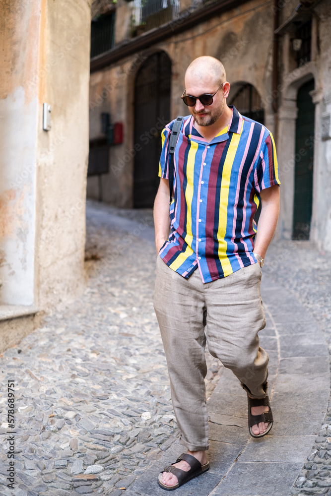 A man in a colorful shirt and loose pants enjoys his vacation in the south of Italy. He strolls through the streets and has an old black camera with him. He looks relaxed and in a good mood. A man in a colorful shirt and loose pants enjoys his vacation in the south of Italy. He strolls through the streets and has an old black camera with him. He looks relaxed and in a good mood.