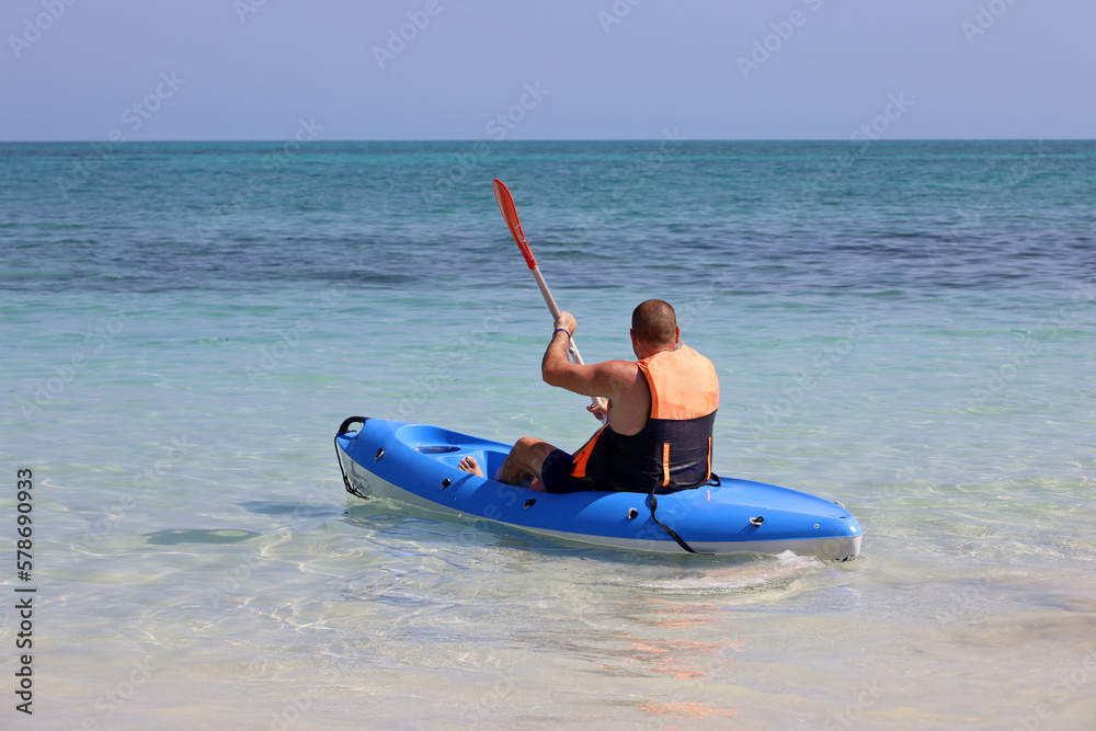 Kayaking in the sea, man wearing life vest sitting with paddle in canoe. Travel and water sports concept