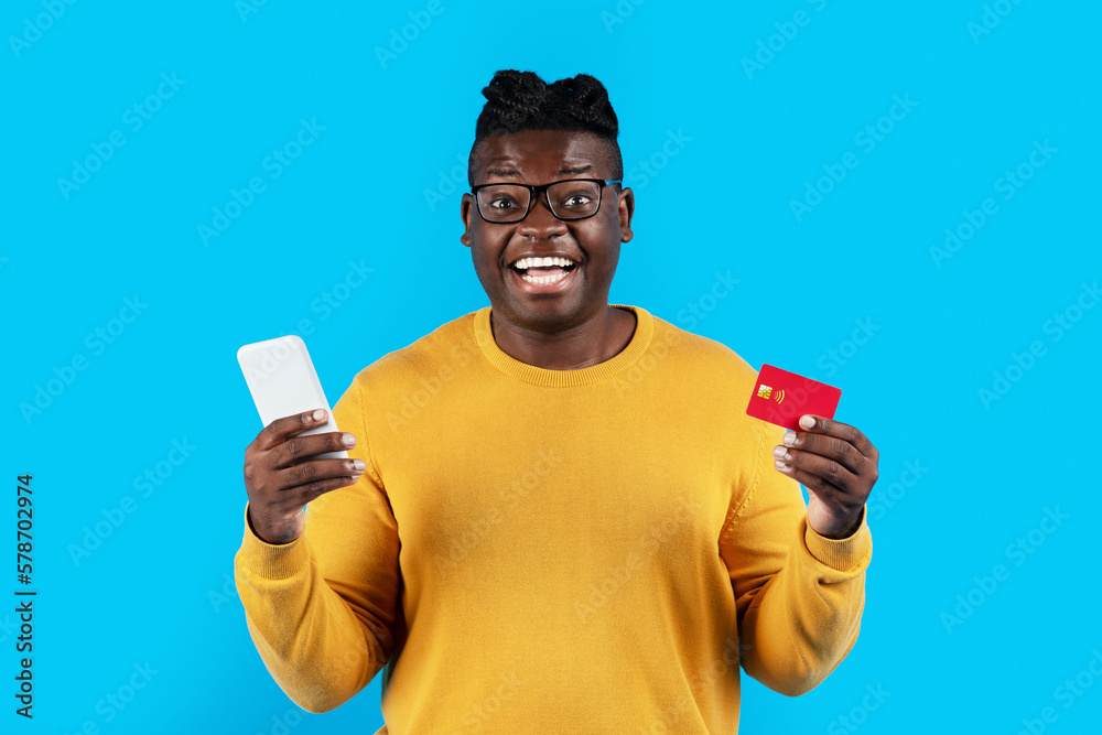 E-Commerce Concept. Excited Young Black Man Holding Smartphone And Credit Card E-Commerce Concept. Excited Young Black Man Holding Smartphone And Credit Card