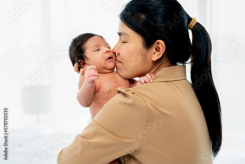 Close up Asian mother hold newborn baby and kiss with love and care in room with white curtain and day light.