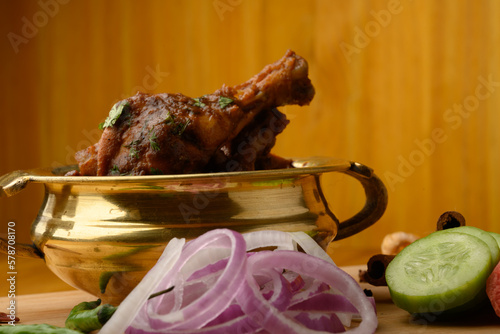 Spicy Reddish saoji Chicken Curry  Masala served in brass bowl or Kadhai ,with prominent Leg Piece, different spices and salad like cucumber onion carrot over  wooden background. photo