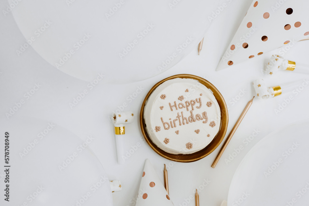 Birthday cake with sign "Happy Birthday", balloons, candles, party hats. White and gold colours. Flat lay, top view. - obrazy, fototapety, plakaty 