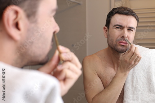 Man using tweezers to pluck nose hairs 