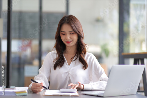 Young beautiful asian businesswoman in office working with laptop and financial documents on desk.