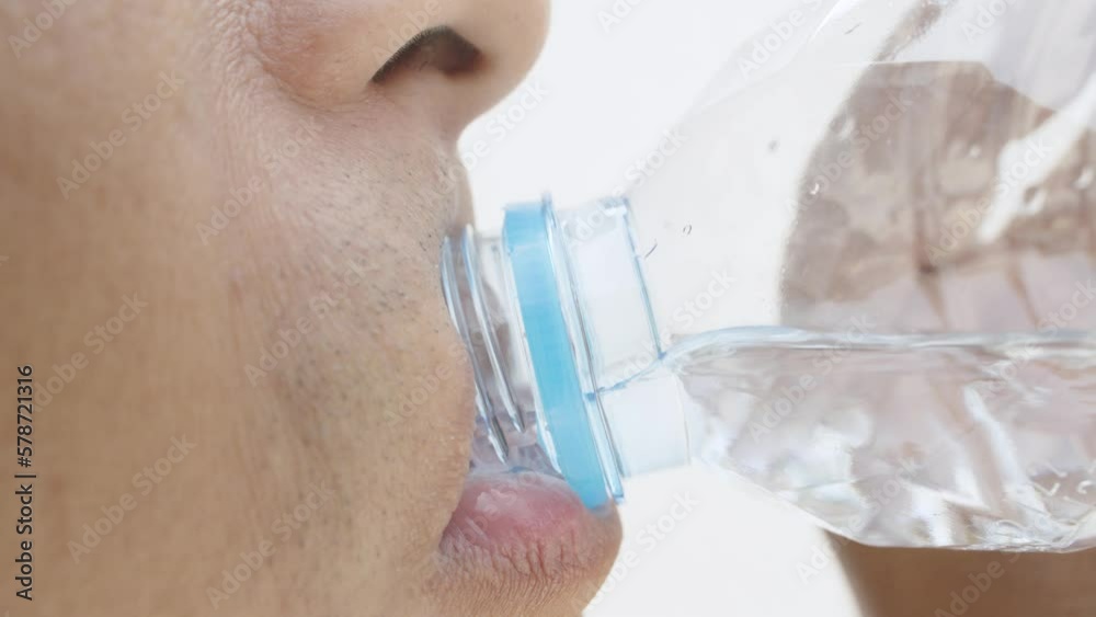 Thirst quenching, Drink clean water from a plastic bottle. Man of Asian appearance drinks water from a transparent plastic bottle against white background, Close-up. Thirst quenching, Drink clean water from a plastic bottle. Man of Asian appearance drinks water from a transparent plastic bottle against white background, Close-up.