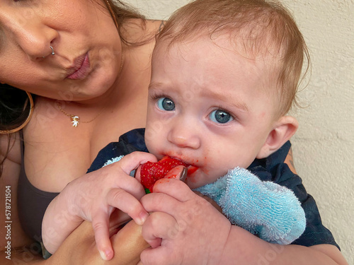 Mother feeding her blue-eyed baby an organic strawberry photo