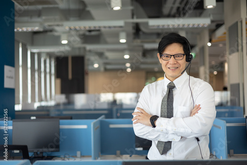 Portrait of smart asian male customer service representative with headset  smile face and stand at call center room.