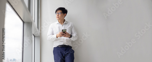 Handsome office worker hold mobile phone in hand chat with girlfriend by mobile phone looking out through window at modren office balcony in relax time.