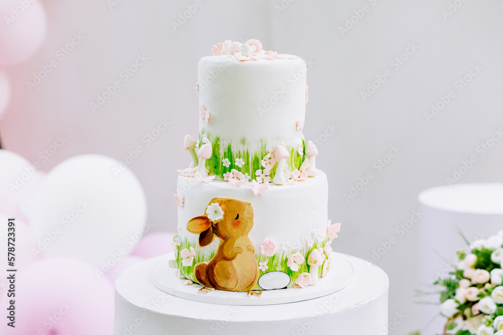 Tasty white birthday cake of a little girl in front of a pastel-colored background with balloons