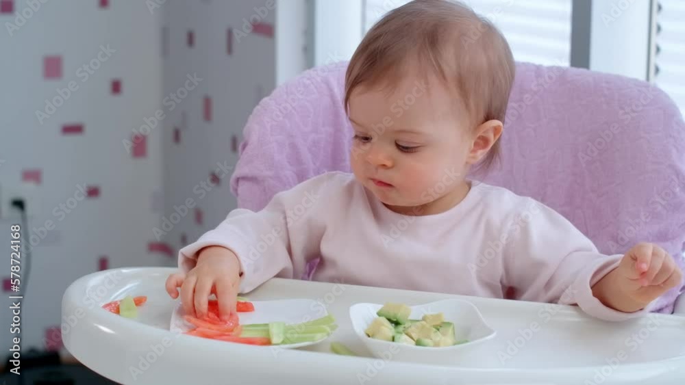 Toddler baby girl eating lunch by herself and throwing food on the floor in the kitchen, weaning. Toddler baby girl eating lunch by herself and throwing food on the floor in the kitchen, weaning.