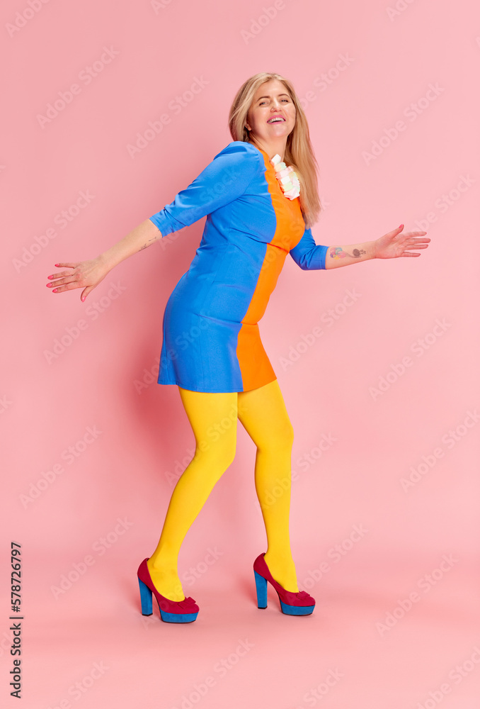 Full-length portrait of happy smiling woman in colorful clothes with yellow tights on heels posing, dancing against pink studio background. Concept of emotions, facial expression, lifestyle, fashion Full-length portrait of happy smiling woman in colorful clothes with yellow tights on heels posing, dancing against pink studio background. Concept of emotions, facial expression, lifestyle, fashion