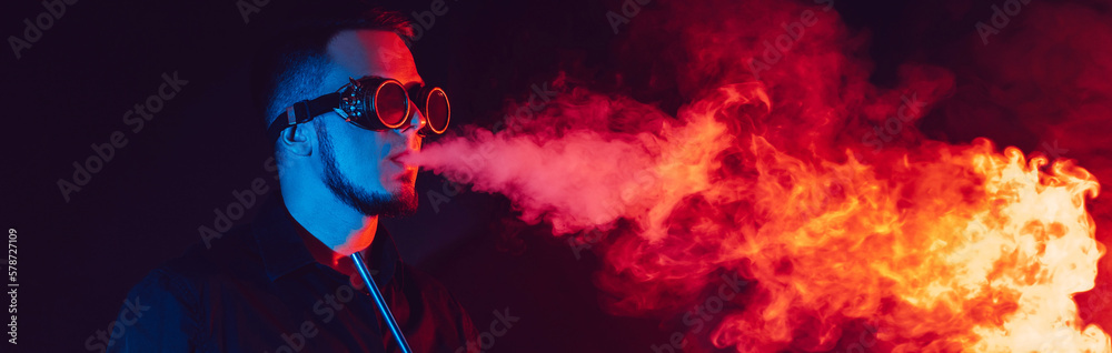 man in futuristic glasses smokes a hookah and blows a cloud of smoke in a shisha bar with red and blue neon lights
