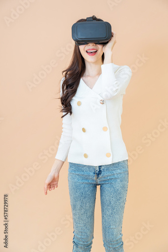 portrait of a young asia woman wearing a white cardigan and VR glasses. She is amazed by what she is seeing. Virtual reality headset. isolated orange background