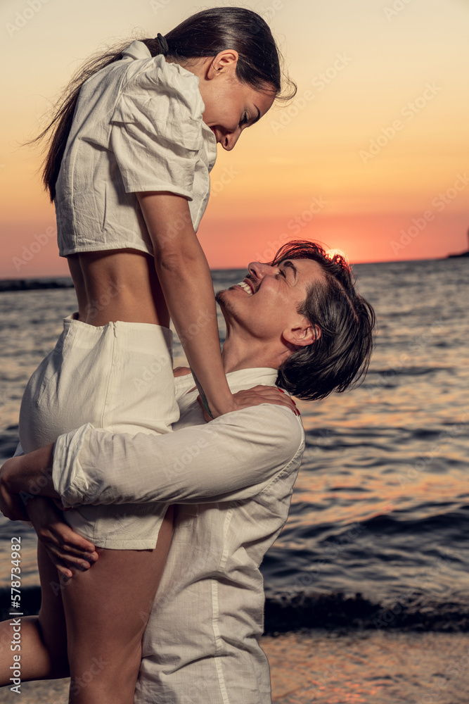 Photoshoot of young helthy beautiful couple, boy and girl, dating at the beach - Man and woman lovers dancing near the ocean in a sunny day looking at each others